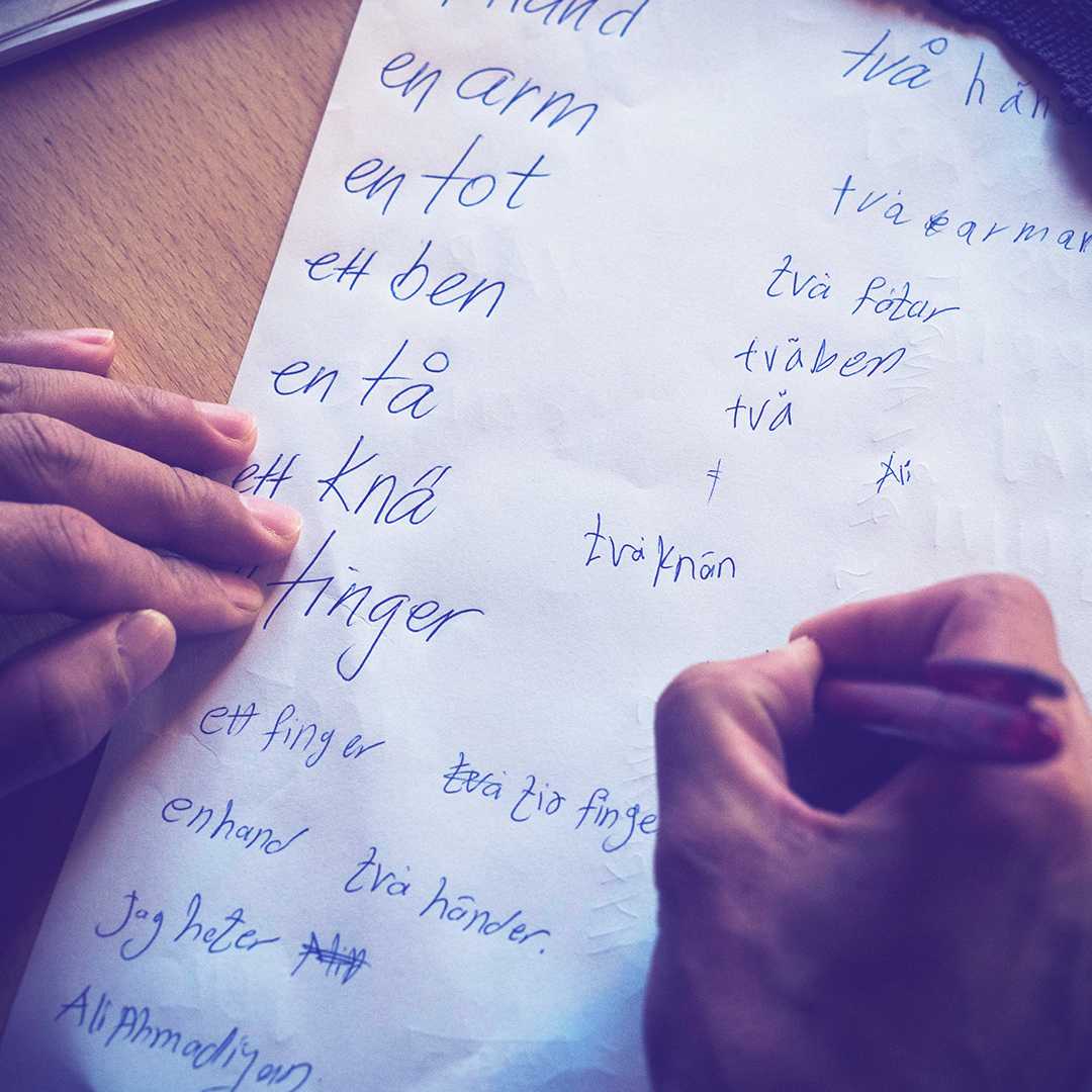 Händer som skriver svenska ord på ett papper